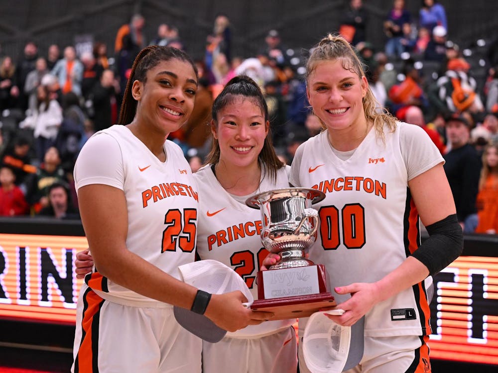 Three women pose in their basketball jerseys with a trophy, with a blurry crowd in the background.