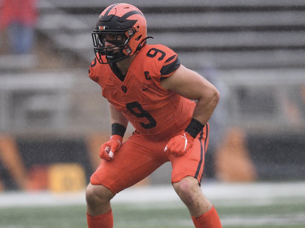 A football played in an orange and black uniform crouches on a field.