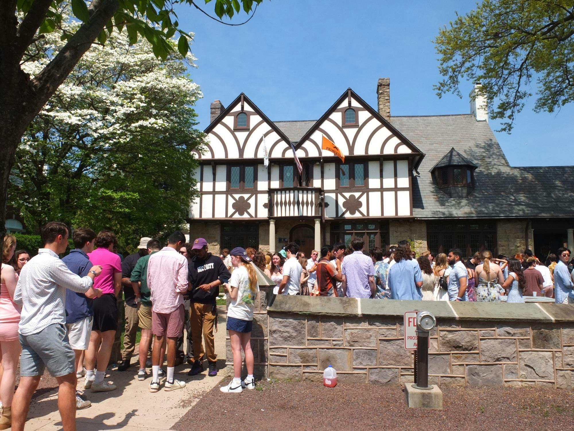 A Tudor-style house overlooks a crowd of people dancing in the front yard. 