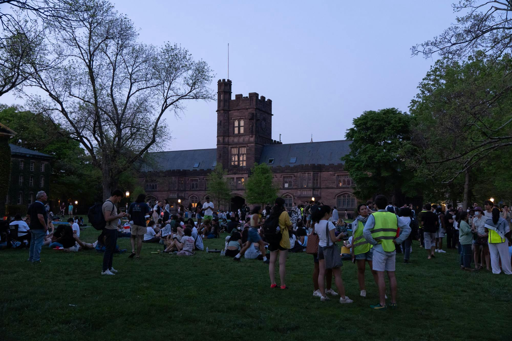 People gather on lawn in front of brownish-red brick building.