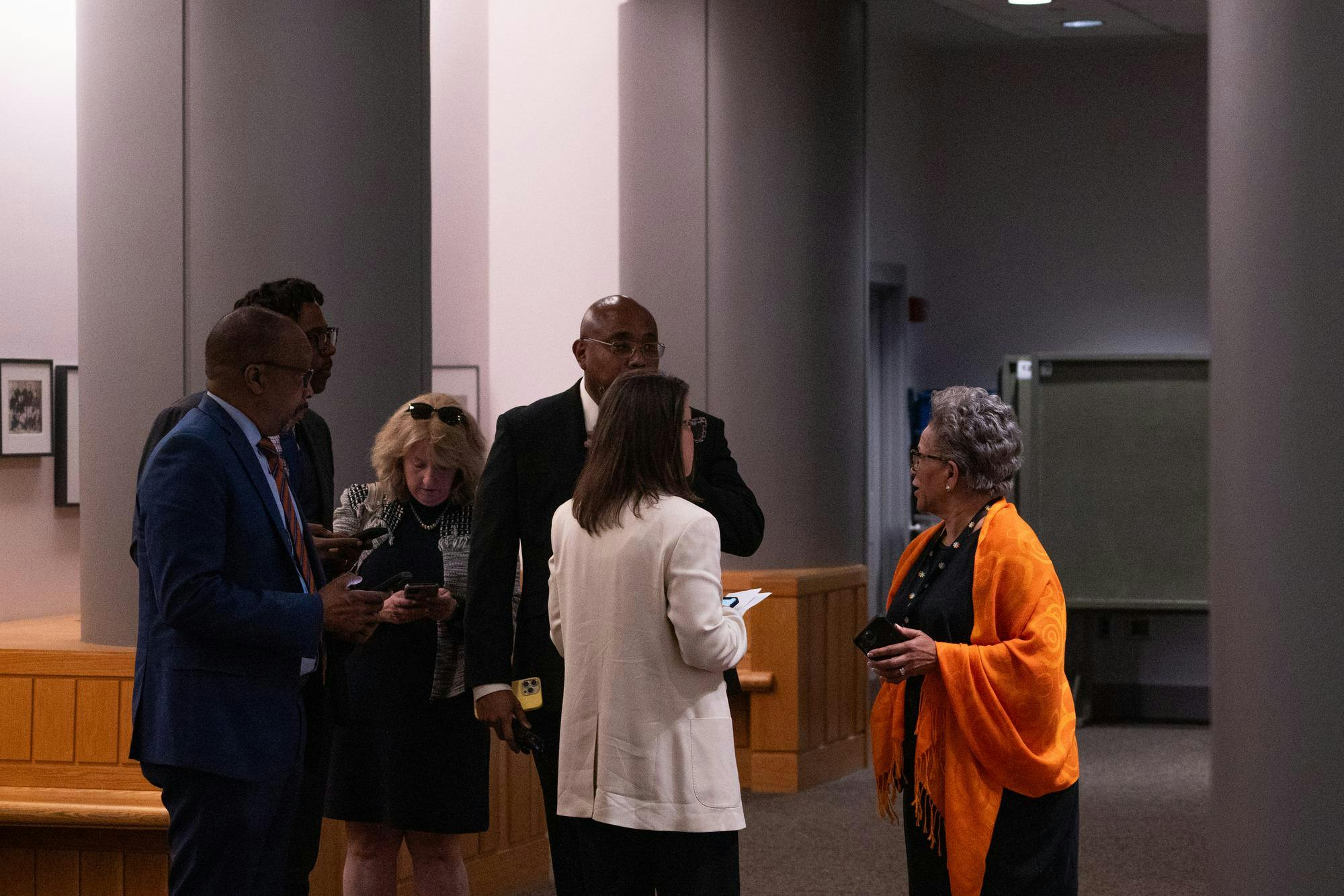 Six well dressed people huddle in discussion in a dark room. 