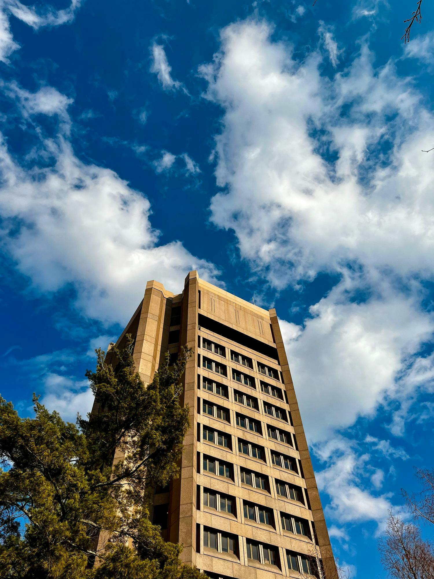 Large tan stone building extending into the blue sky with wispy white clouds above.
