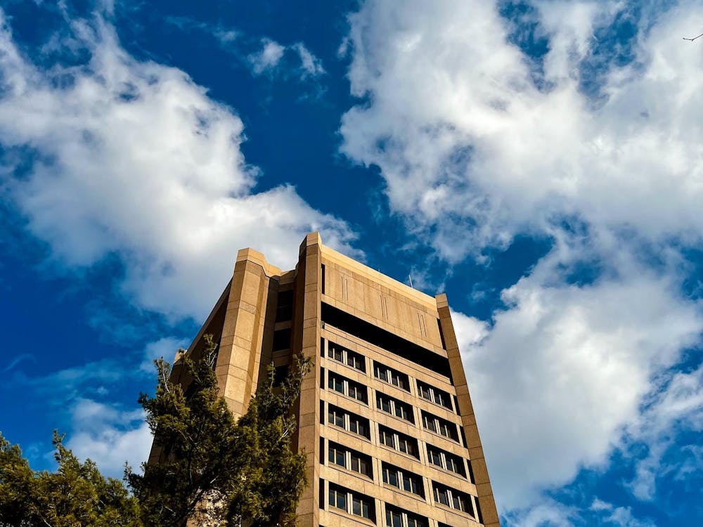 Large tan stone building extending into the blue sky with wispy white clouds above.