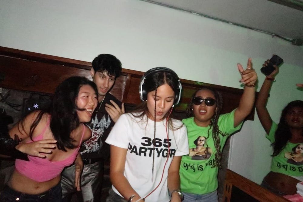 Three students cheering behind a girl DJing.