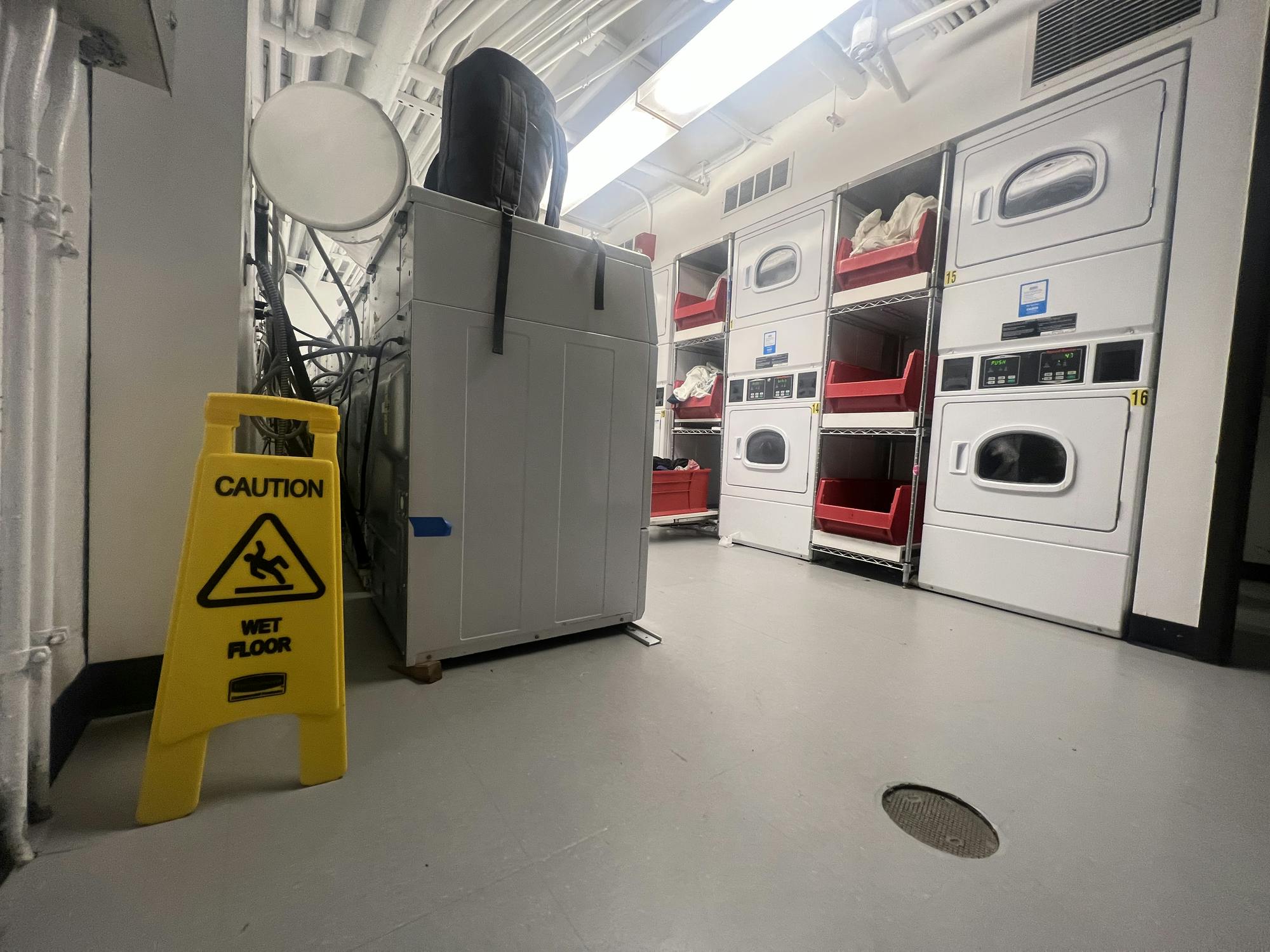 A brightly-lit laundry room with stacked units and a yellow caution sign.
