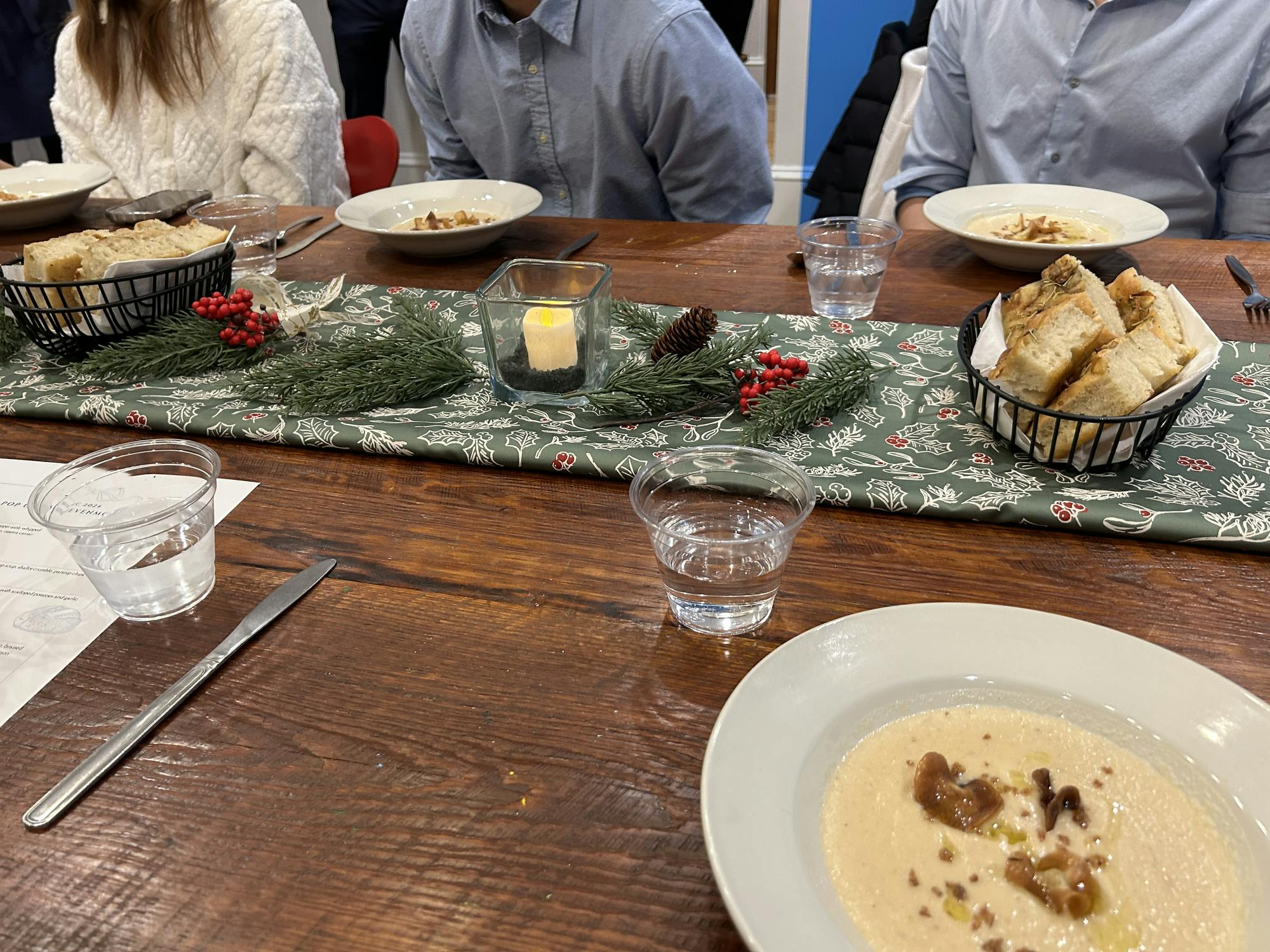 Mistletoe table runner, a candle, pine needles laid out on a dark wooden dining table. 