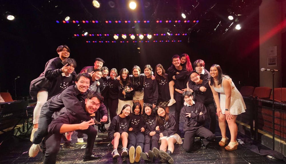People wearing black t-shirts pose in a photo on a black stage.