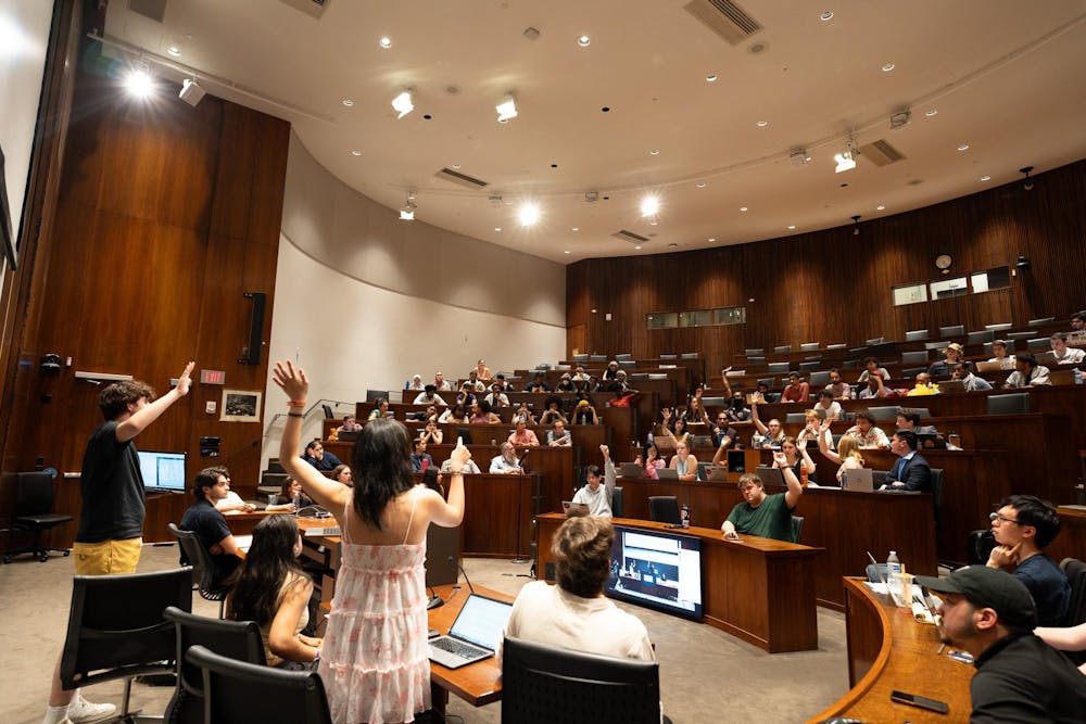 A large group of students in an auditorium with some students raising their hands to signal their affirmative votes.