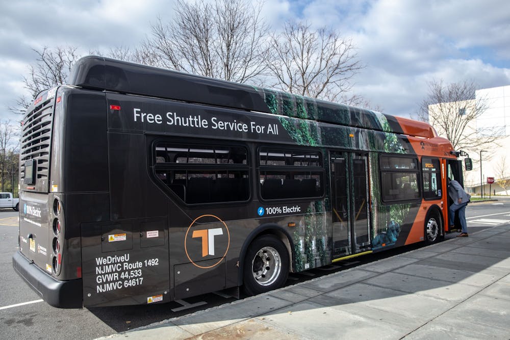 A black-and-orange bus on a sunny day has the words “Free Shuttle Service For All” on its side.