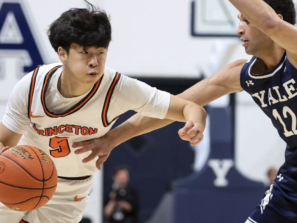 A Princeton player in a white jersey dribbling a basketball, being guarded by a player in a blue jersey.