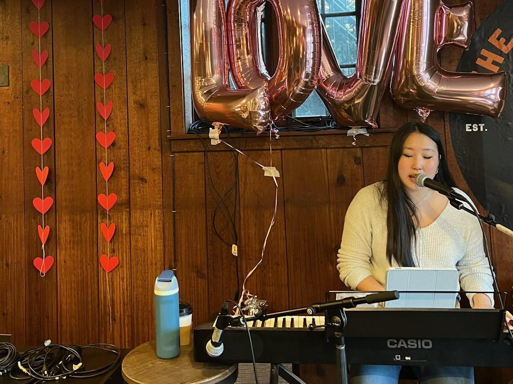 A girl with a white sweater plays a black keyboard in a room decorated with hearts. 