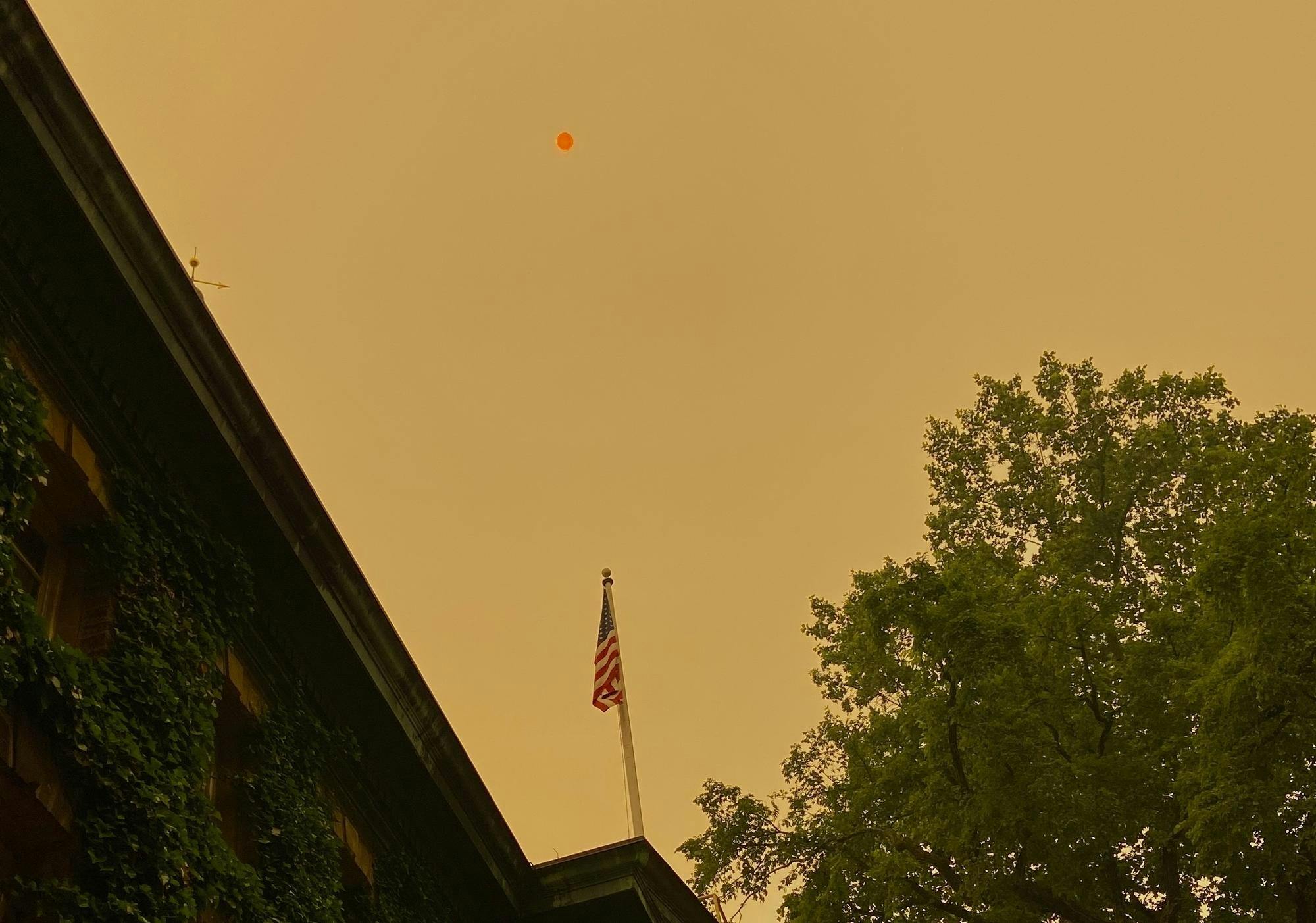 The American flag on Nassau Hall flies in front of an orange sky with a very red sun.