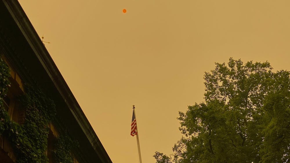 The American flag on Nassau Hall flies in front of an orange sky with a very red sun.