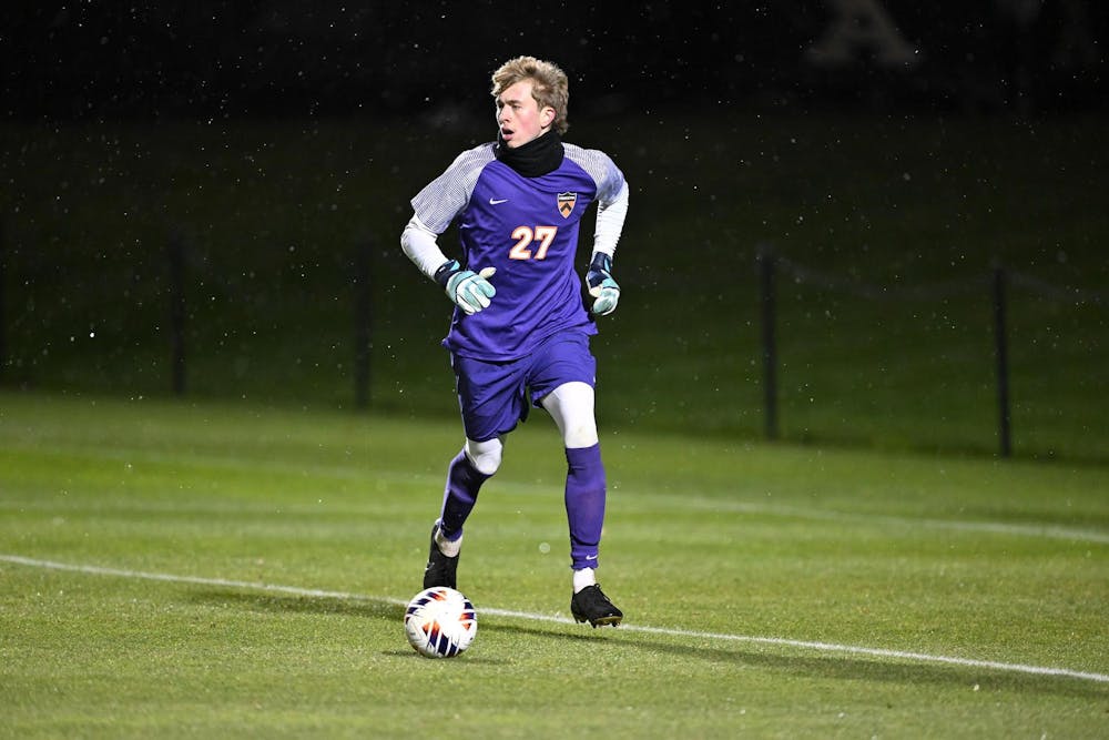 A goalkeeper wearing purple attire kicking a soccer ball on a grass field during a match