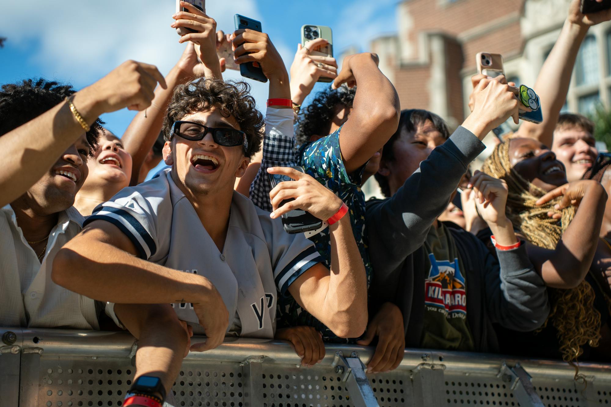 Students carrying smartphones cheer next to a silver barricade. 