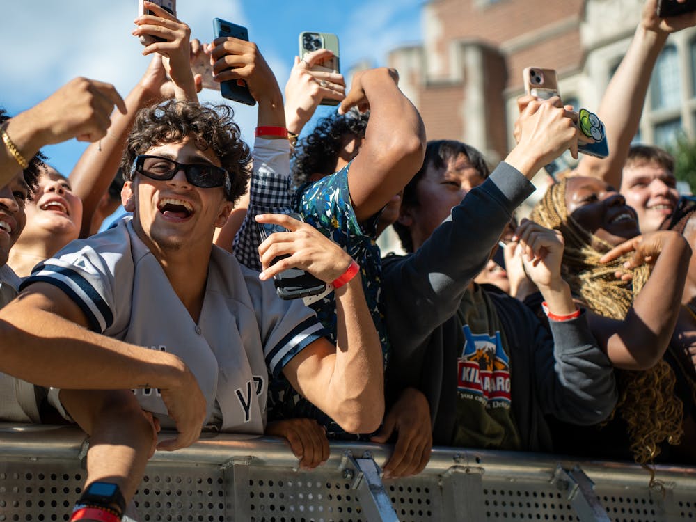 Students carrying smartphones cheer next to a silver barricade.