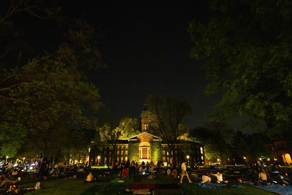 Nassau Hall at night with Cannon Green, full of students milling around.