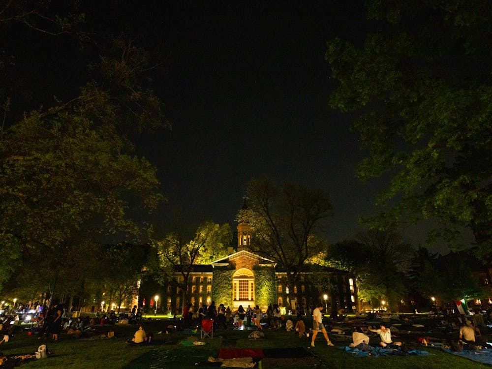 Nassau Hall at night with Cannon Green, full of students milling around.