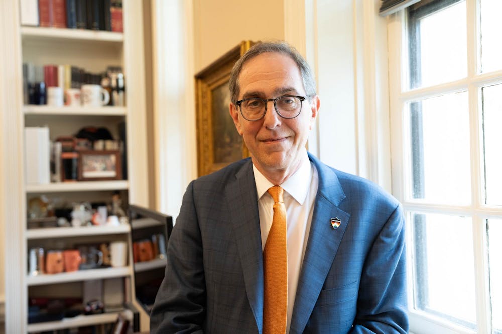 Man with blue suit and orange tie posed in front of bookshelves and window.