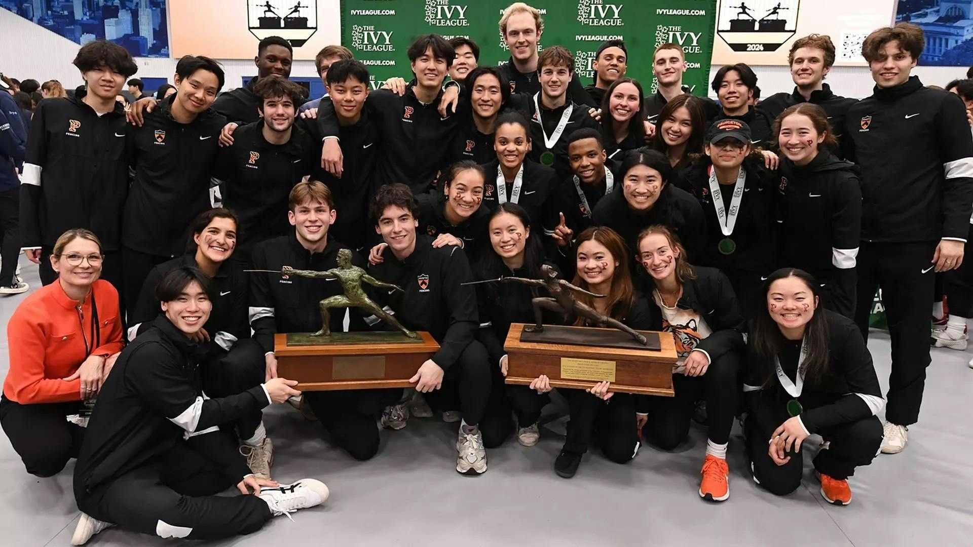 A group of men and women fencers standing together with two trophies in the middle of the picture. 