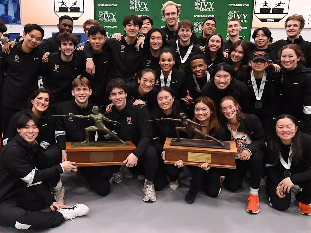 A group of men and women fencers standing together with two trophies in the middle of the picture. 
