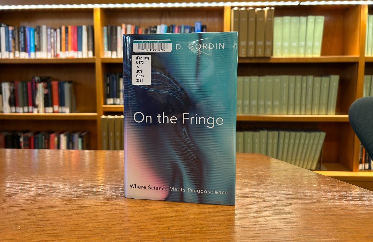 A book on a table in front of a shelf of books at a library.
