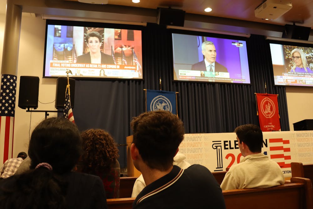 Three screens are at the top of the image, showing three different political shows. A group of students are clustered around, watching.