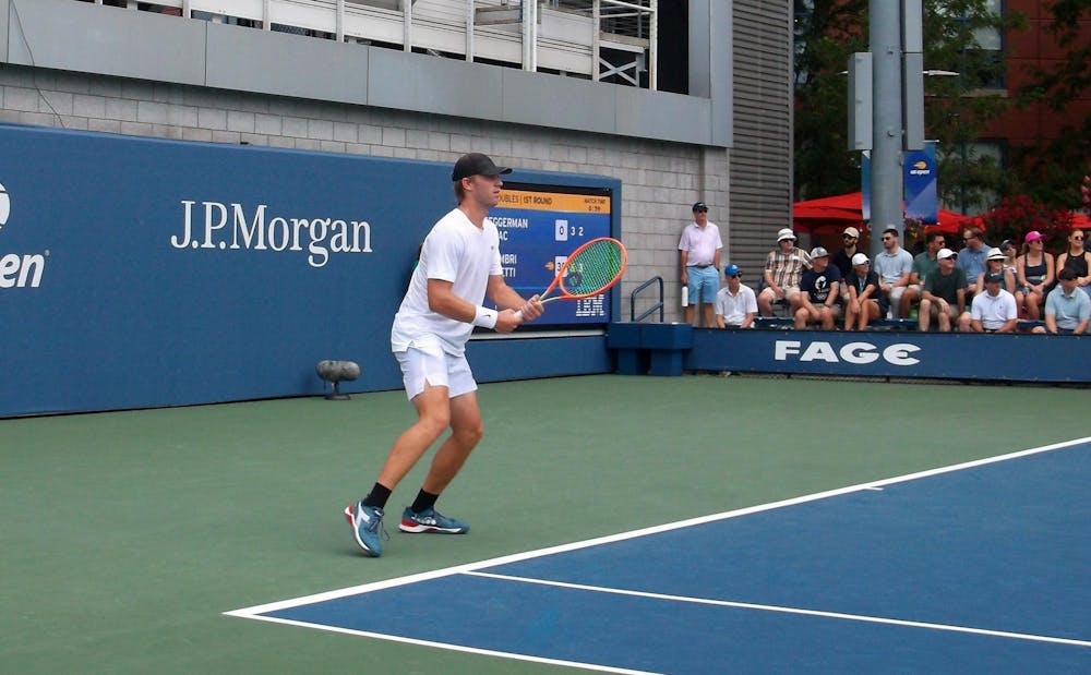 Man in white shirt prepares to return tennis serve