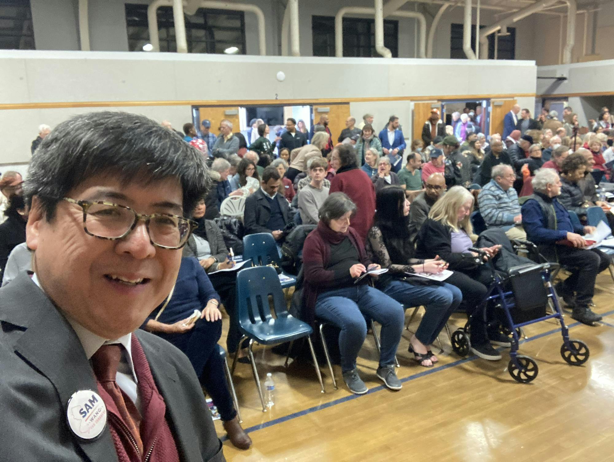 A photo of an Asian man standing against a backdrop of people.