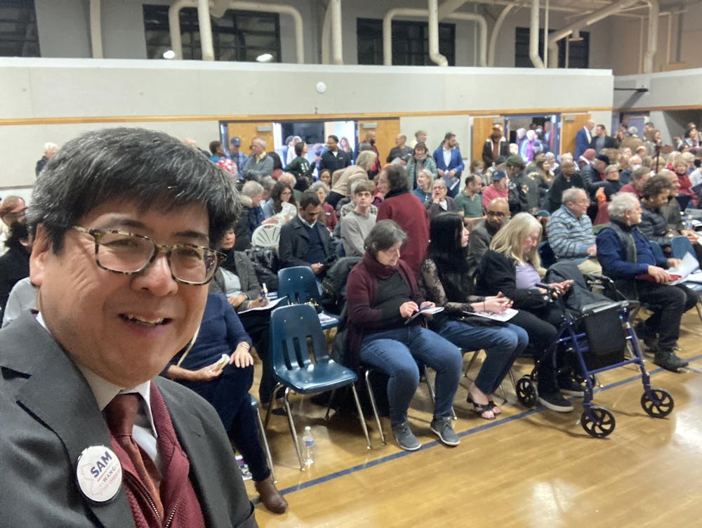 A photo of an Asian man standing against a backdrop of people.