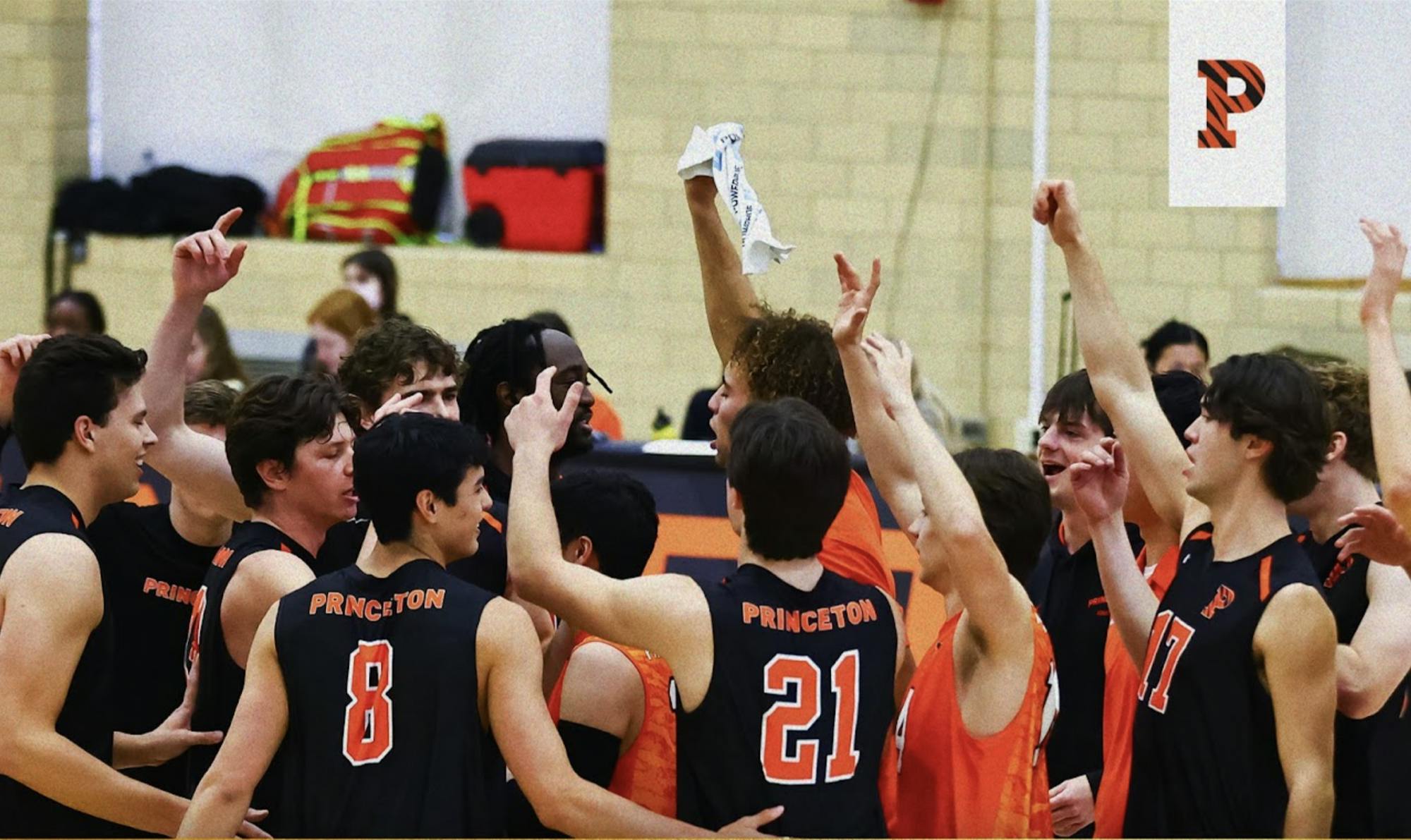 Men’s volleyball players in black jerseys gather on the volleyball court with arms raised in celebration.