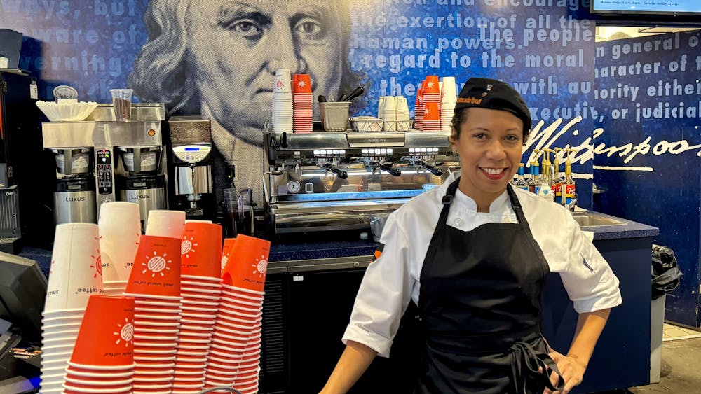 A woman in a white shirt and black apron poses in front of an espresso machine.