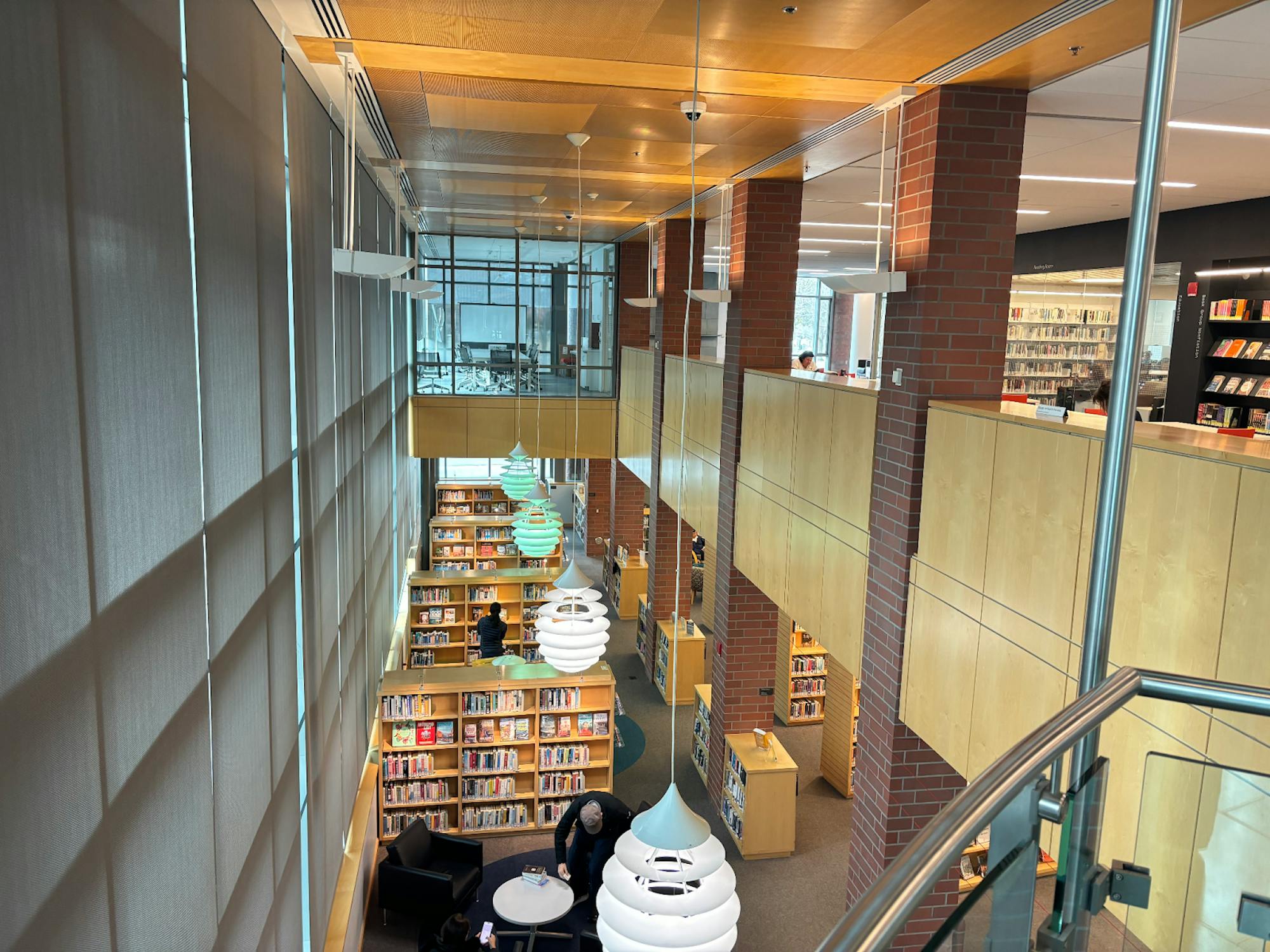 Bookshelves with patrons wondering around on a lower floor, and workspaces and conference rooms on the upper floor. 