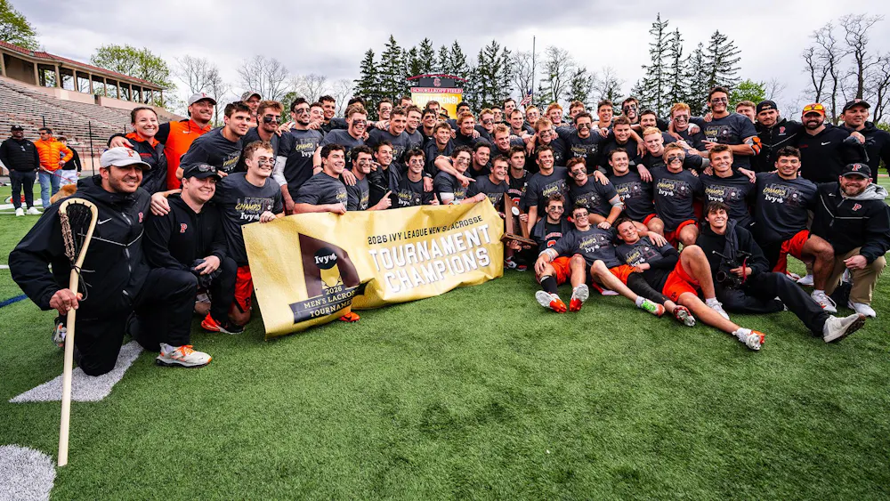 A group of players and staff pose with a tournament trophy on a grass field.