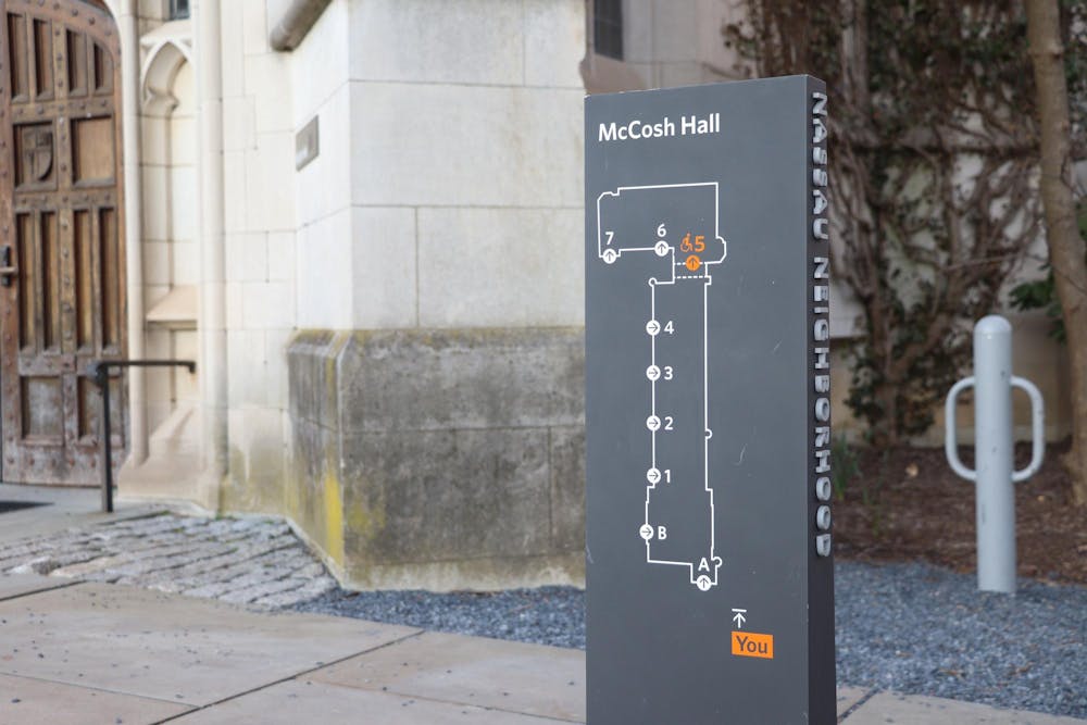 Grey sign with a map on it in front of a grey stone building.