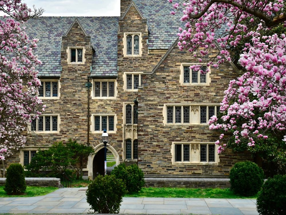 A photo of a gothic building in springtime on an overcast day. The building has a dozen windows, and trees with pink flowers surround the building. 