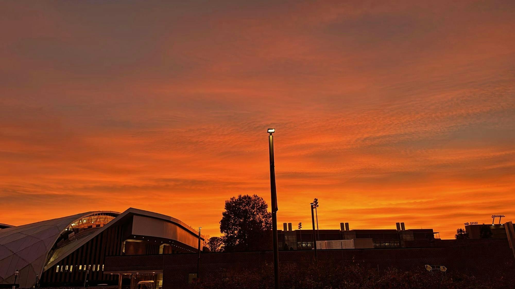 An orange and red sunset sky over a gymnasium on a university campus. 