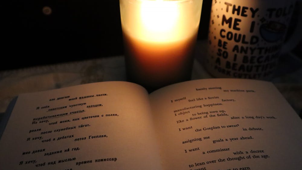 By candlelight sits an open book. On the left is Mayakovsky’s poetry in Russian and on the right, the English translation. Next to the candle is a mug with the following text written in black bubble letters "They told me I could be anything, so I became a [unintelligible text]"