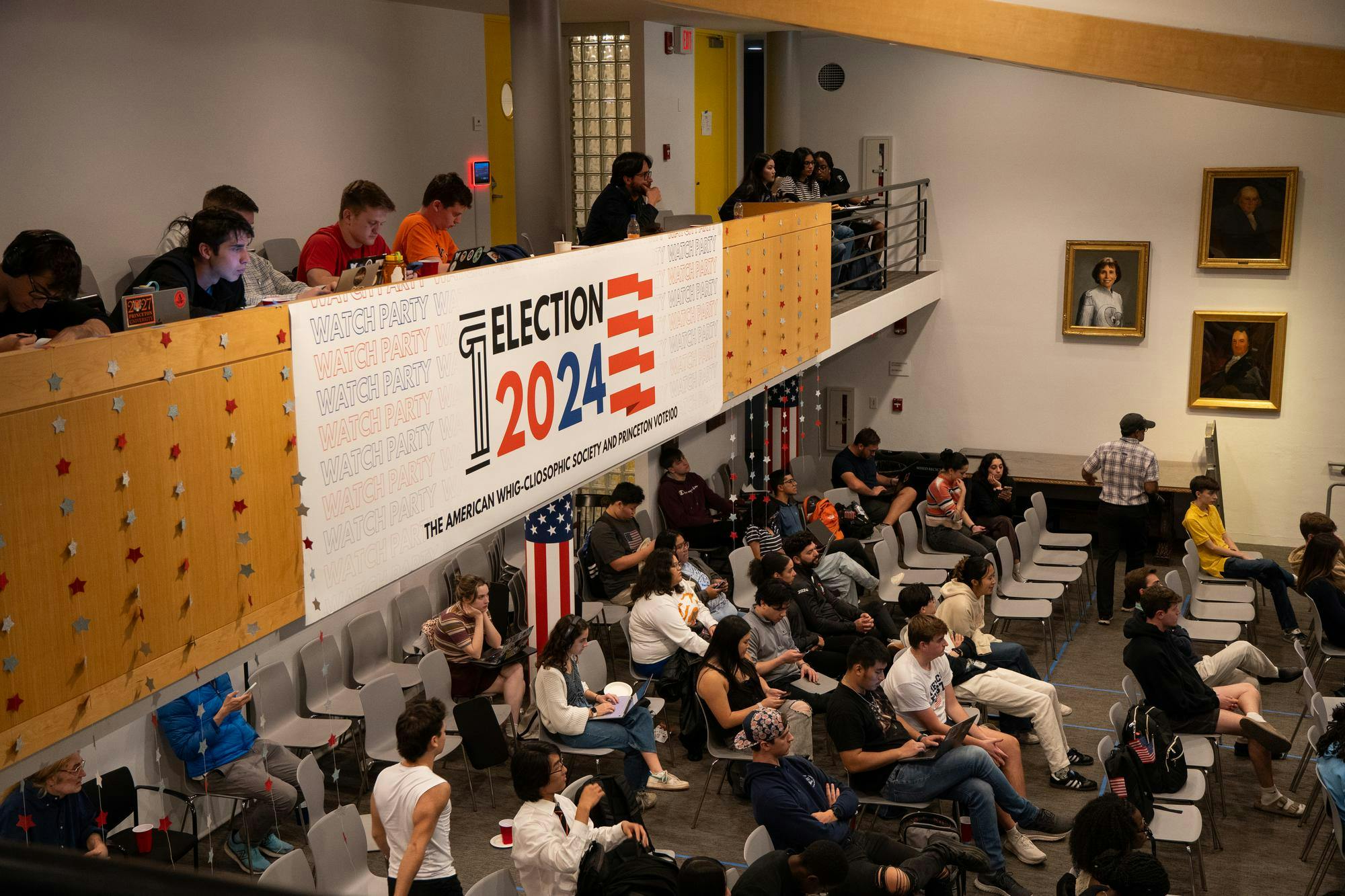 "Election 2024" banner hang over an indoor balcony. Students sit on rows of chairs.