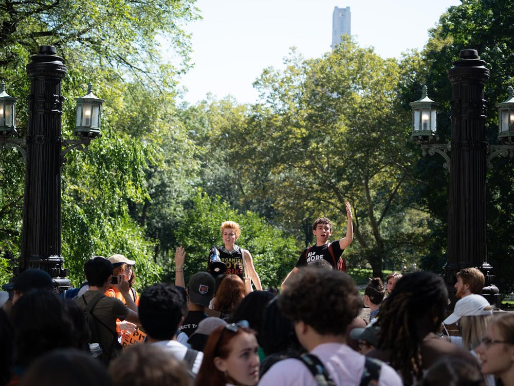 Two people, one holding a megaphone, stand in front of a crowd of people holding signs in a park.