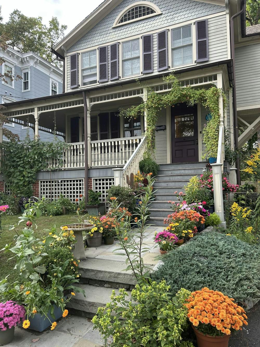 A light blue house with a whale plaque by the front door and a staircase that has many colorful flowers lining either side.