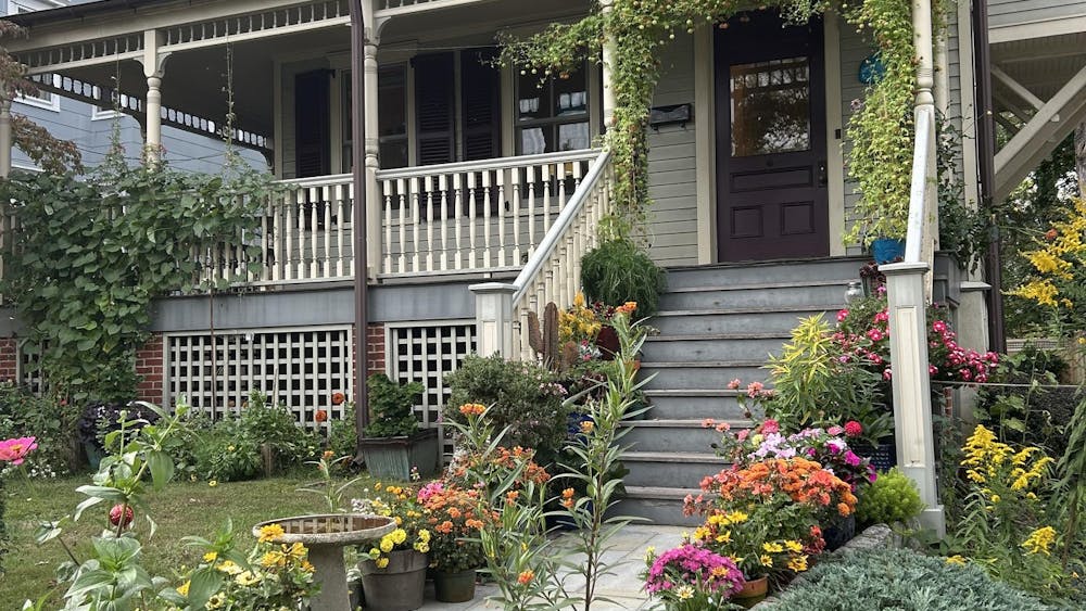 A light blue house with a whale plaque by the front door and a staircase that has many colorful flowers lining either side.