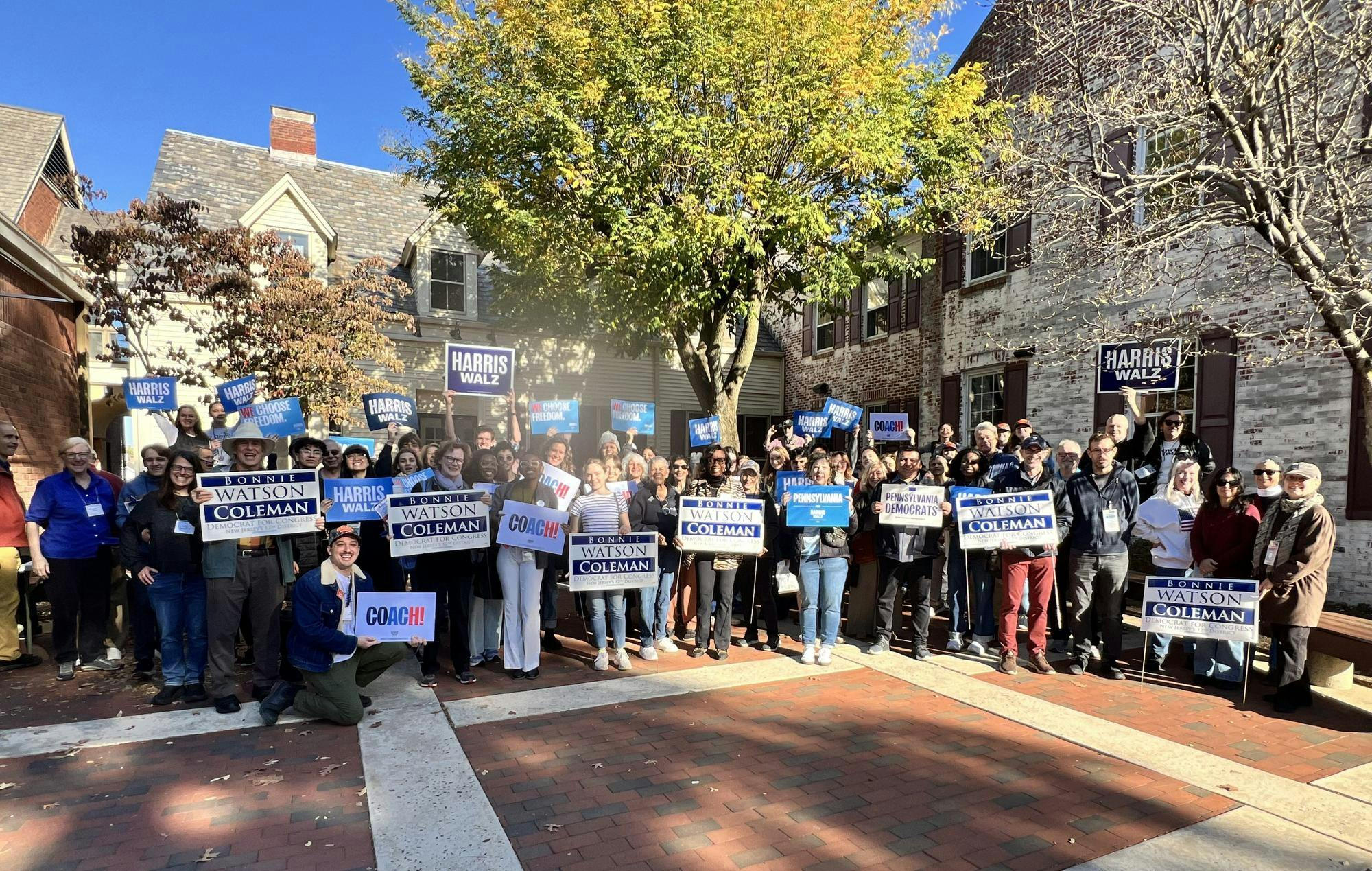 A group of around fifty people stand in a square with signs that read "Bonnie Watson."