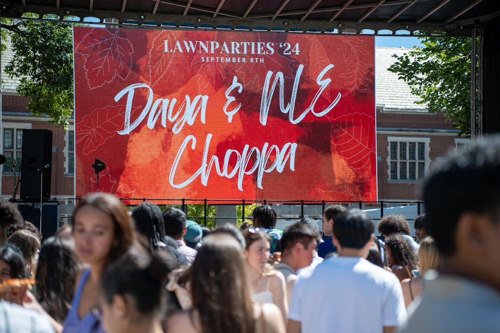 Students wait in a crowd in the foreground. A poster reading “Lawnparties ‘24, September 8th, Daya & NLE Choppa” hangs on stage.