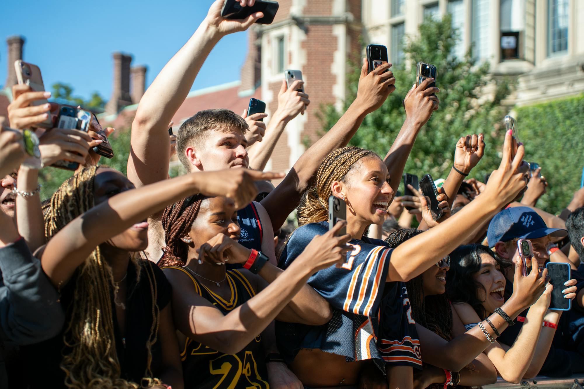 Row of students line up on a barricade holding their smartphones up.
