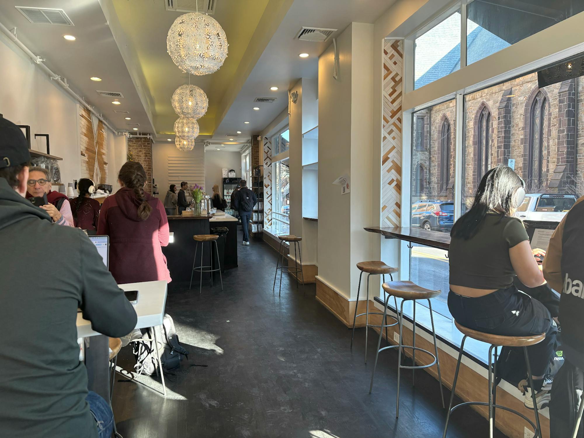 Counter seating and high tables with barstools for customers, with the ordering counter in the back, inside of a coffee shop.