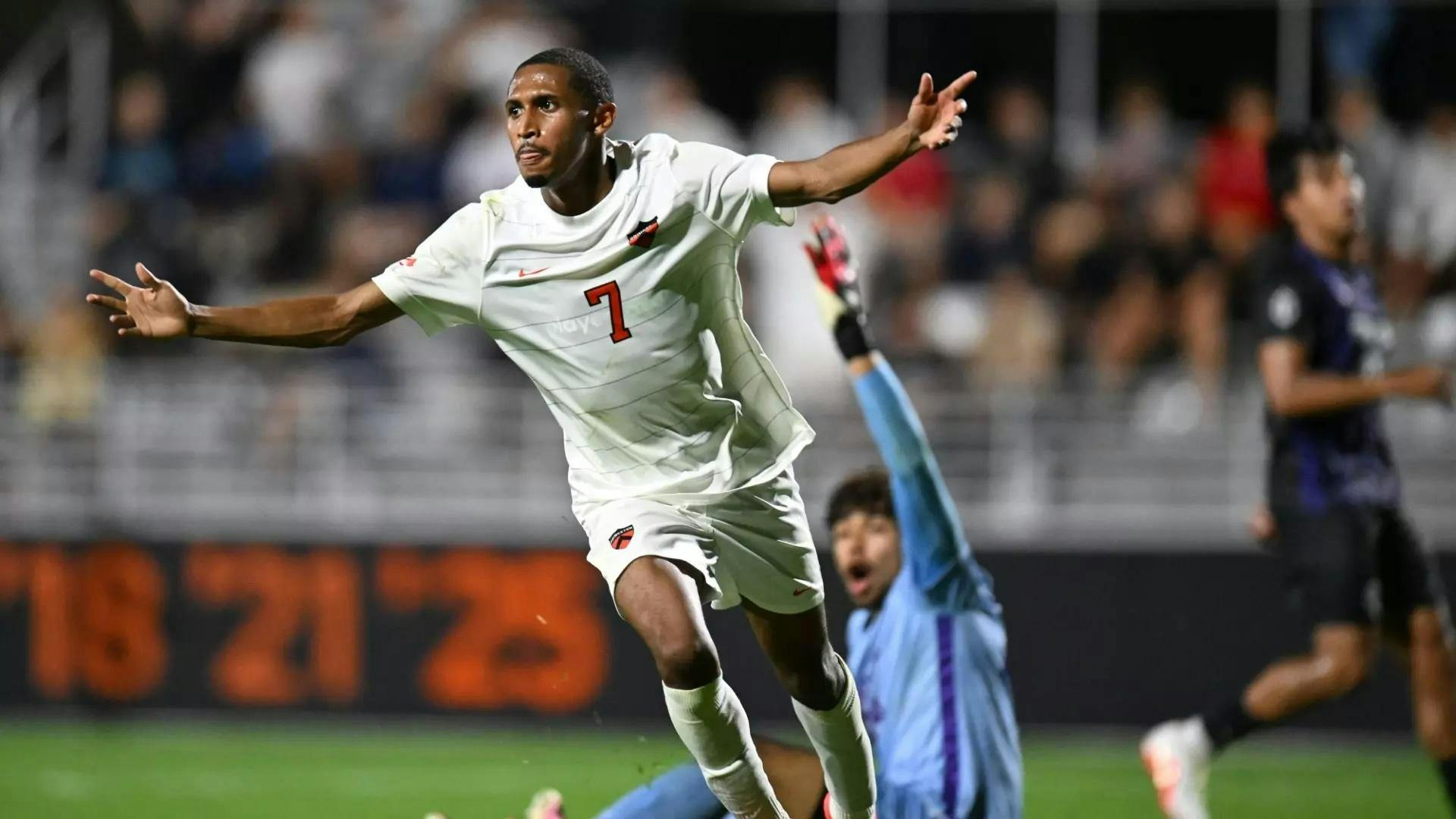 A soccer player in a white and orange jersey is celebrating after scoring a goal.