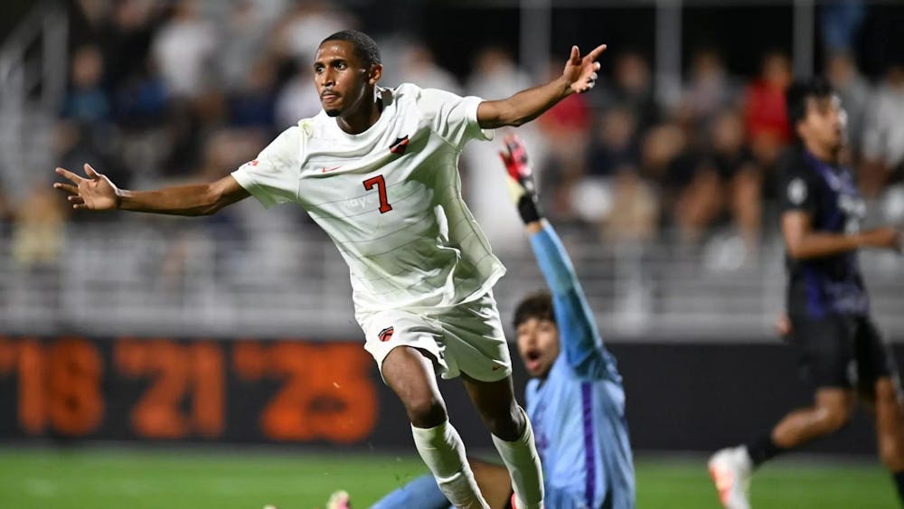 A soccer player in a white and orange jersey is celebrating after scoring a goal.