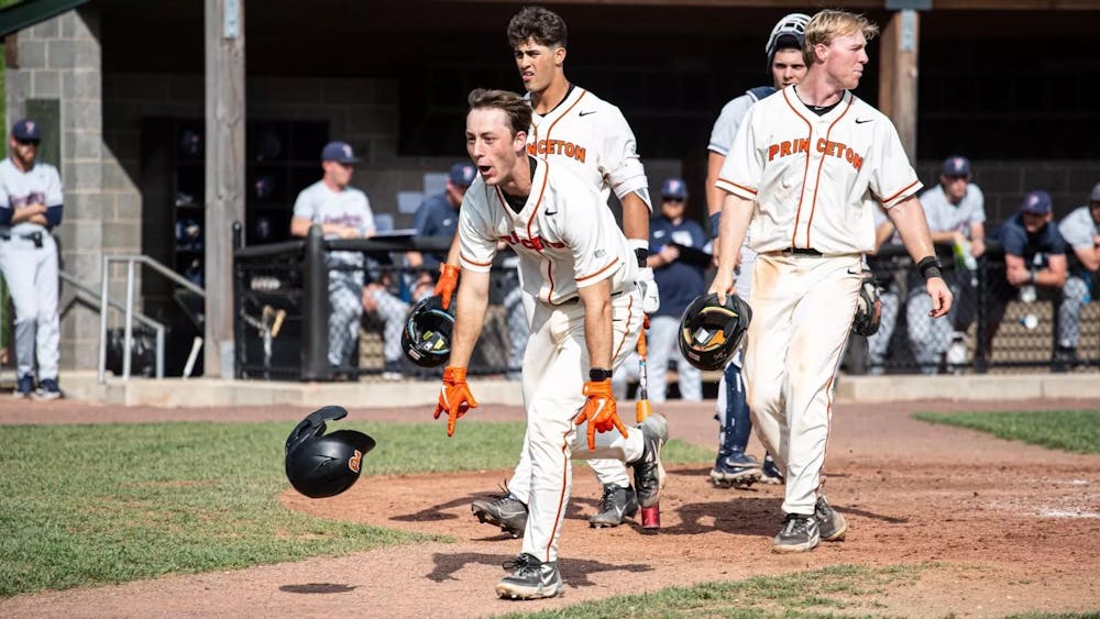 Princeton baseball player in a white jersey celebrates and runs into the field.