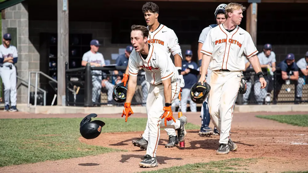 Princeton baseball player in a white jersey celebrates and runs into the field.